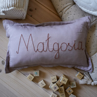 Zdjęcie różowej lnianej poduszki z falbaną, spersonalizowanej z napisem. Poduszka ma wymiary 50 x 30 cm i jest wykonana z wysokiej jakości materiałów: poszewka z 100% lnu i wypełnienie z antyalergicznego włókna poliestrowego.